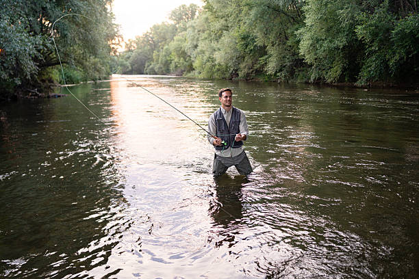 istock Man fly fishing in a scenic river surrounded by lush greenery 2226120601