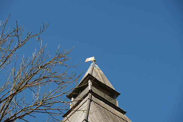 A charming wooden spire reaches towards a bright blue sky. Tree branches extend gracefully, adding a natural frame to the serene setting during daytime.