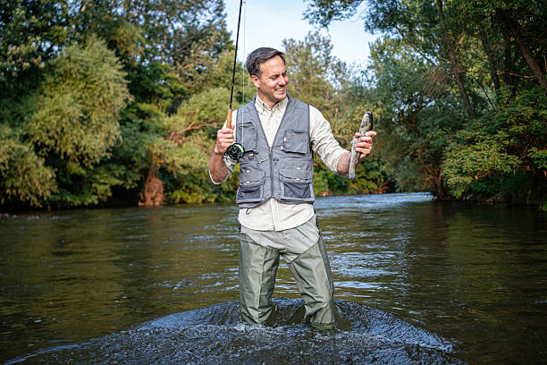 istock Man fly fishing in a tranquil river surrounded by lush greenery 2226122061