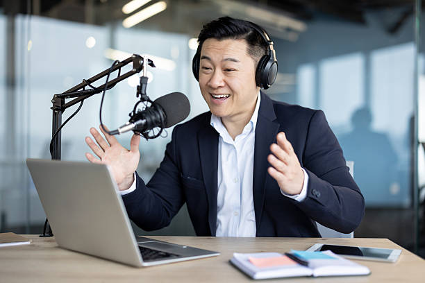 istock Asian man enthusiastically recording a podcast in a modern office studio with a microphone and laptop. 2226123439