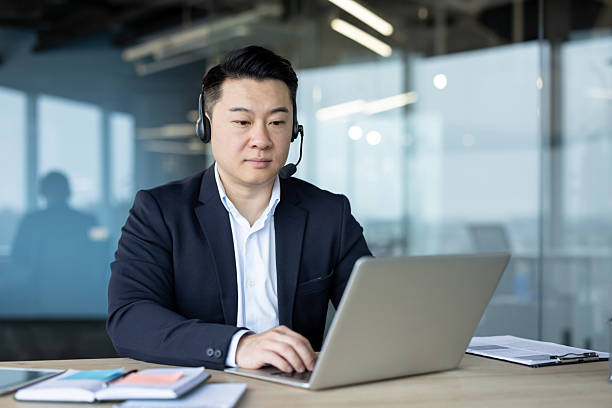 istock Focused asian businessman using a laptop in a modern office setting while wearing a headset. 2226129001
