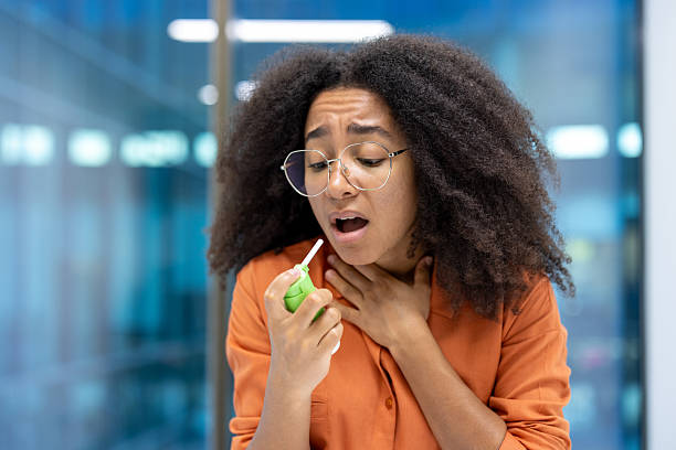 istock A young woman with glasses using a throat spray, concerned expression, holding her neck. 2226129645