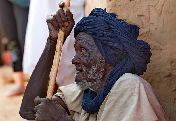 Mhaireth, Mauritania. October 05, 2021 Portrait of a very elderly Moorish man with a blue turban on his head sitting in the shade of a village hut near the oasis.