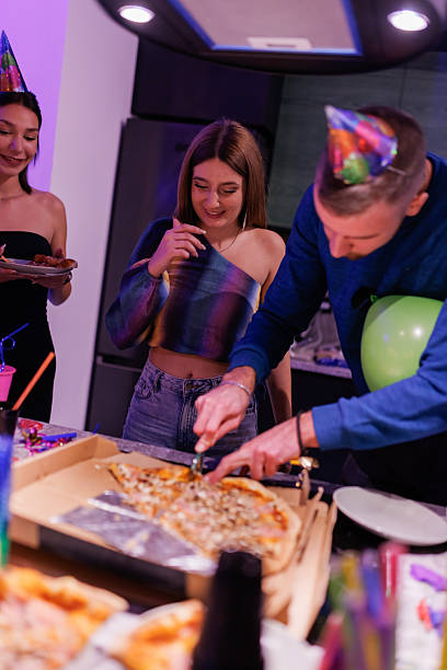 Friends celebrating a birthday party with pizza and festive hats in a colorful kitchen setting