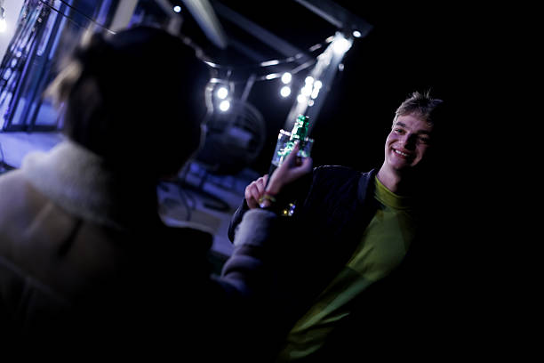 Two friends share a joyful moment toasting drinks during a nighttime hangout in a warmly lit outdoor setting adorned with festive string lights, symbolizing friendship, celebration, radiant happiness.