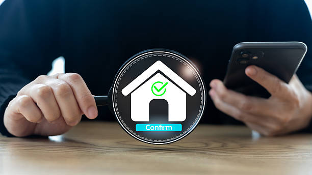 istock Hand holding a magnifying glass and smartphone with a house icon and confirm button, representing mobile property verification, real estate approval, and digital home inspection. 2226133922