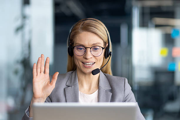 istock Friendly woman in a headset waves hello during an online video call from her office setting. 2226134855