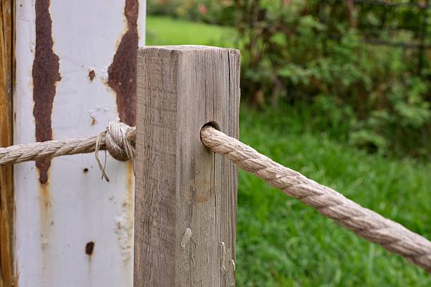 A wooden post with a rope tied to it. The rope is tied to a post on the other side of a fence