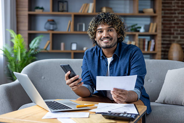 istock A cheerful man reviews bills and uses his phone while working from home. 2226138695
