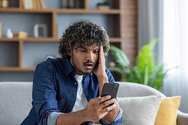 istock A worried man looks at his phone while sitting on the couch at home. 2226143349
