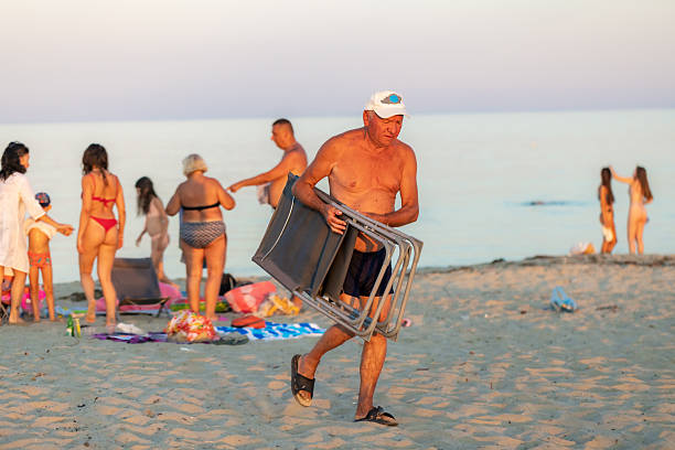 Walking along the beach, a street vendor sells music and movies to tourists enjoying their summer holidays. The vibrant scene captures the essence of vacation leisure and outdoor fun