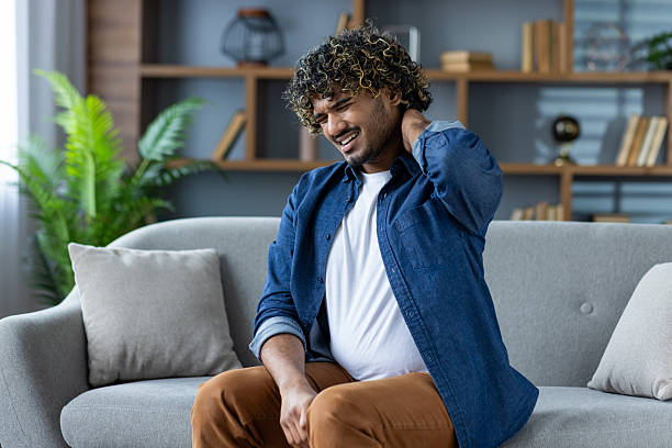 istock Man experiencing neck pain while sitting on a sofa inside his living room. 2226146226