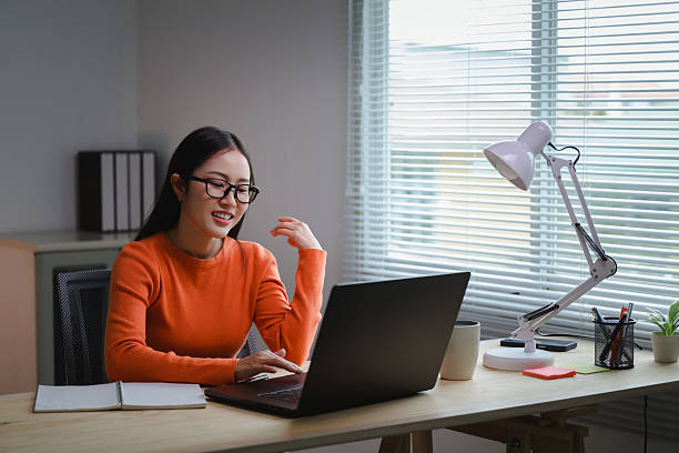 istock Young Asian woman smiling while working from home, focused on her laptop at a modern desk, enjoying a productive day filled with creativity 2226156458