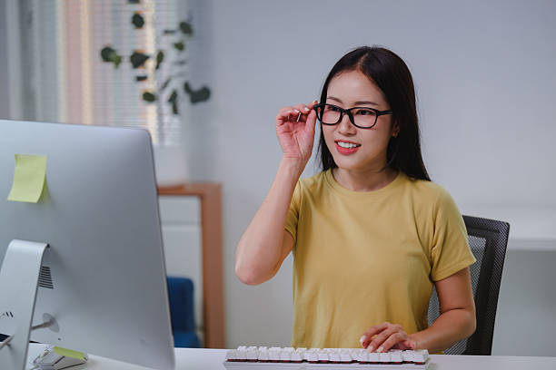 istock Young Asian woman working from home at a desktop computer, adjusting her glasses while focused on typing and managing tasks 2226156540
