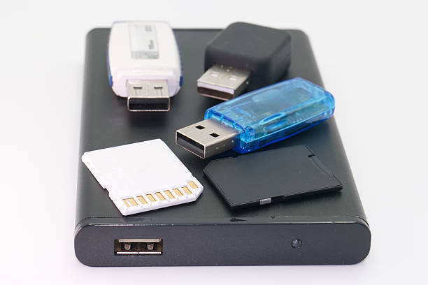 Different types of data storage devices, including USB drives and a memory card, are arranged on a black portable hard drive against a white backdrop, showcasing technology and data storage solutions.