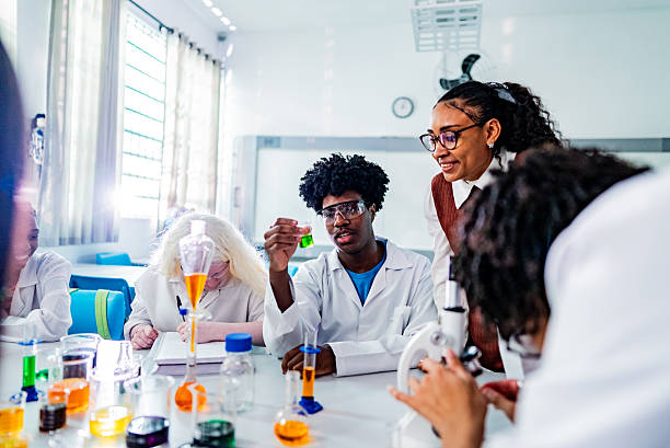 Teacher assisting students with chemical experiment of microscope used in laboratory - including albino person