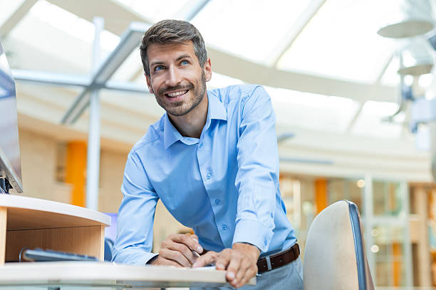 istock Happy businessman taking notes while working in modern office, standing by his desk, using a modern computer and writing something on a piece of paper 2226167492