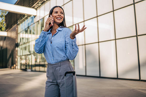 istock Businesswoman talking on phone while walking with suitcase 2226189915