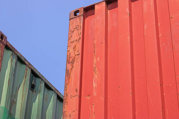 Red and green partial shipping containers against blue sky industry and commerce background.