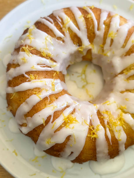 Stock photo shows a delicious lemon drizzle cake in a ring-shaped Bundt tin, topped with glossy icing dripping down the sides and decorated with fresh lemon zest. This homemade cake captures the essence of classic baking with its moist texture and vibrant citrus flavor
