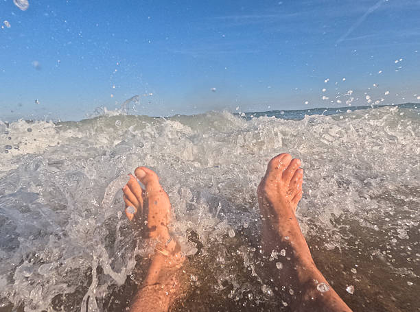Feet of a tourist enjoying the refreshing sea waves on a sunny summer day at the beach, creating user-generated content for a perfect vacation memory
