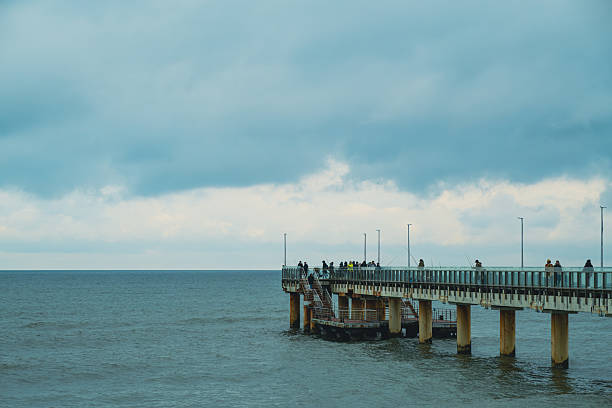 People Walking on a Pier Overlooking the Ocean at Dusk With Dramatic Clouds Above.