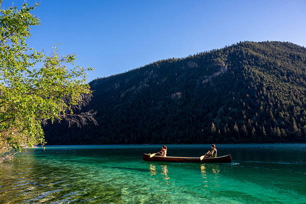 istock Young girls paddle canoe on tranquil mountain lake 2226205584