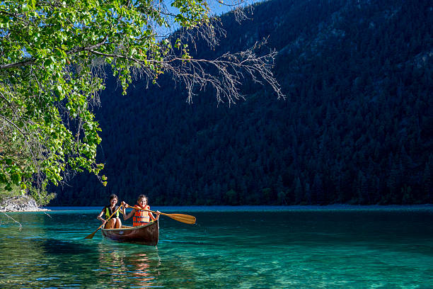 istock Young girls paddle canoe on tranquil mountain lake 2226205903