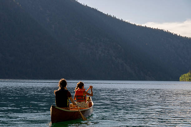 istock Young girls paddle canoe on tranquil mountain lake 2226205957