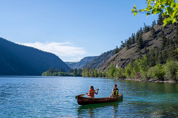 istock Young girls paddle canoe on tranquil mountain lake 2226206144