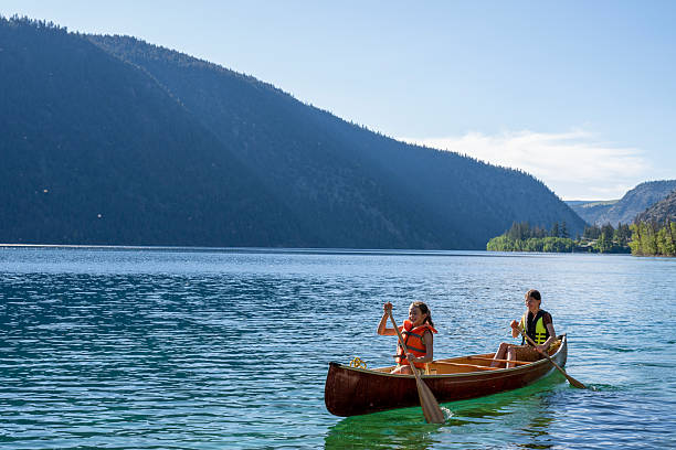 istock Young girls paddle canoe on tranquil mountain lake 2226206283