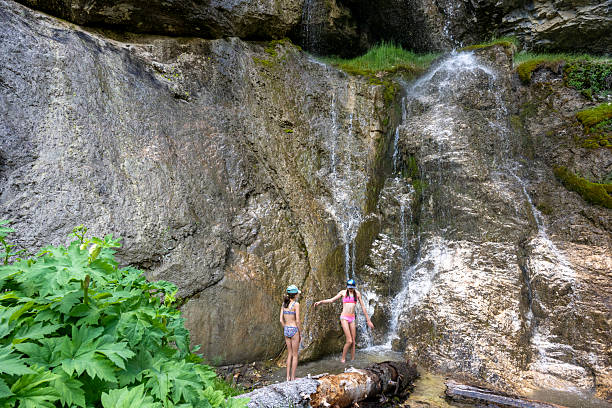 Young girls explore fresh water pool below waterfall in bathing suits, summertime, Whistler, B.C.