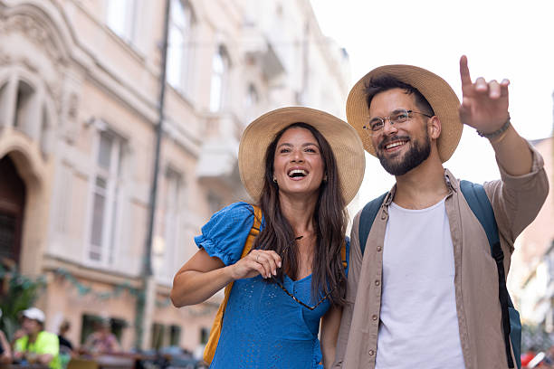 A happy couple wandering romantic urban streets, warmly waving against a backdrop of charming buildings, capturing moments of exploration and shared joy.