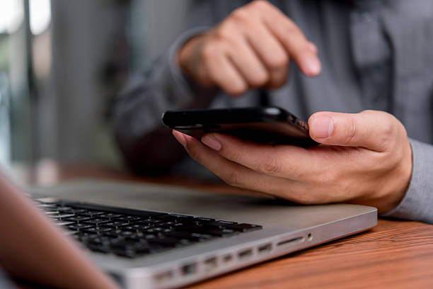 istock Man hand holding a smartphone and touching the screen. Modern business technology, professional person using mobile phone for online communication and work with laptop. Digital lifestyle. 2226216800