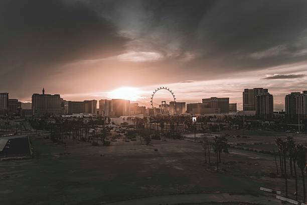 A breathtaking view of a sunset casting a warm glow over a city skyline. The silhouette of a Ferris wheel adds an iconic touch, while dark clouds enhance the dramatic atmosphere. This image captures the essence of urban life and leisure, perfect for themes of travel, adventure, and cityscapes.