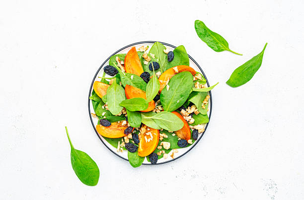 istock Autumn vegan persimmon salad with walnuts, blue raisin and spinach, white background, top view 2226220842
