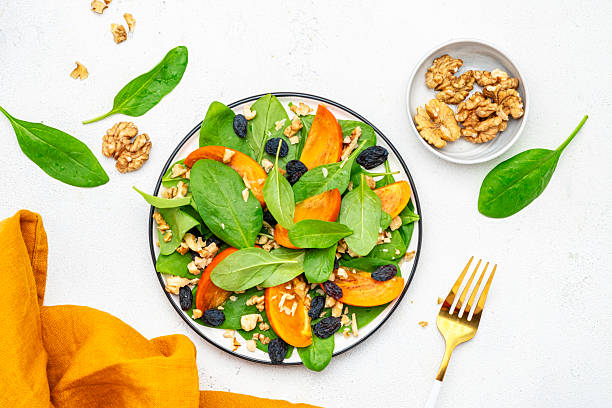 istock Autumn vegan salad with fresh persimmon, walnuts, raisin and spinach, white background, top view 2226220845