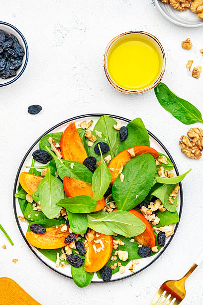 istock Yummy persimmon salad with walnuts, raisin and fresh spinach, white background, top view 2226220848