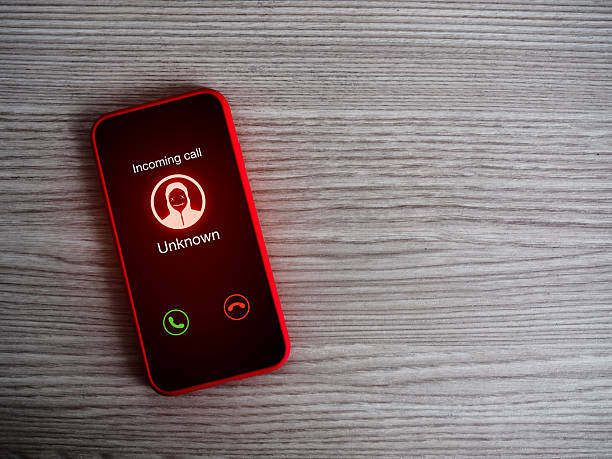 istock Malicious, abusive or threatening calls concept. Incoming call alert with unknown caller, scammer icon, unknown calling display showing on red smart mobile phone screen on wood table with copy space. 2226225330