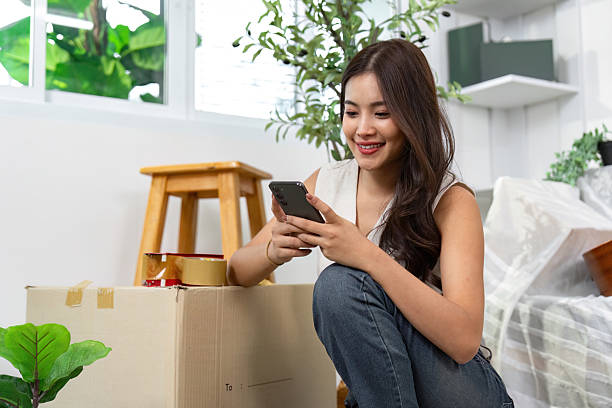 istock Moving house. Woman using her phone while sitting next to boxes. 2226245105