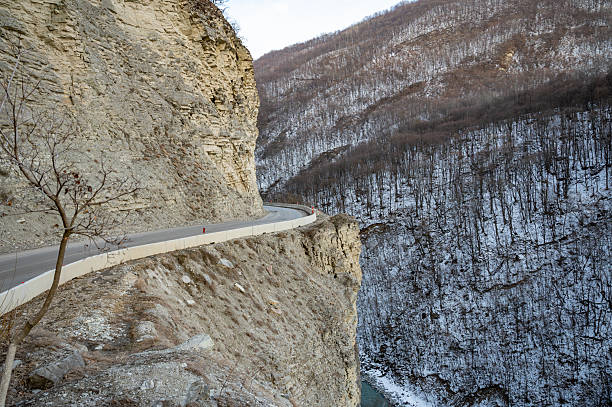 Curving mountain road in the Argun Gorge, framed by rugged cliffs and snowy forested slopes, offering an impressive view of natural beauty and serenity in a winter setting.