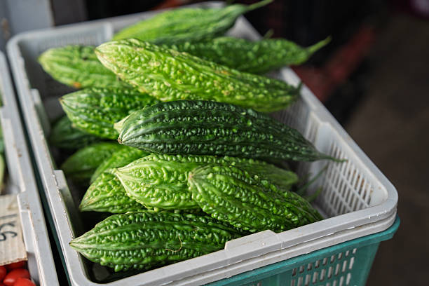 A close-up view of fresh green bitter gourds stacked in a plastic basket, displayed at a local produce market.