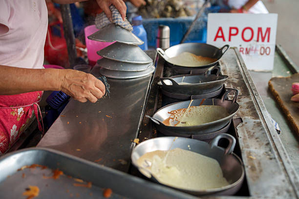 A vendor prepares traditional apom pancakes in multiple small pans at a street food stall, showcasing the local cooking process.