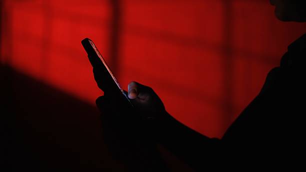 istock Silhouette of a Person Using Smartphone with Vibrant Red Background 2226255295