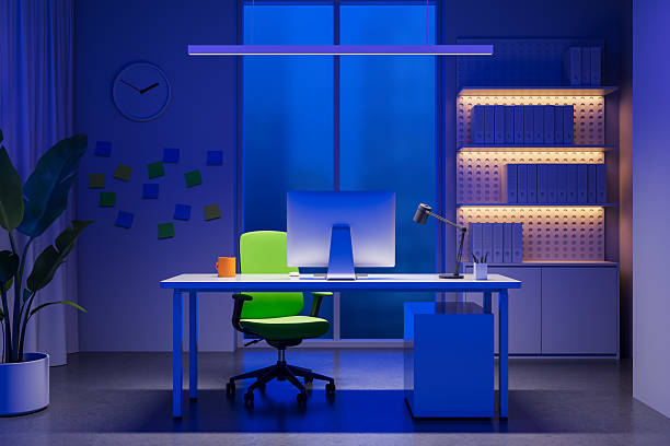 istock Modern office interior with green chair and desktop computer illuminated by moody blue lighting in a contemporary workspace at night. 3D Rendering 2226255835
