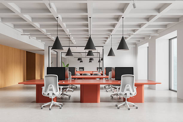 istock Modern open space office interior with red desks, ergonomic white chairs, and geometric ceiling lights in minimalist corporate design setting. 3D Rendering 2226255859