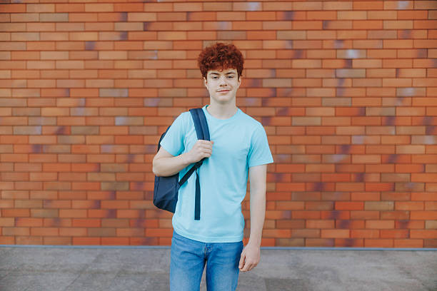 istock Smiling redhead teenage boy outdoors with backpack on colorful brick wall 2226258251