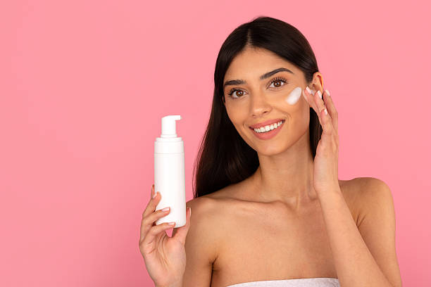 istock Smiling woman applying foaming cleanser on her cheek while holding pump bottle 2226259280