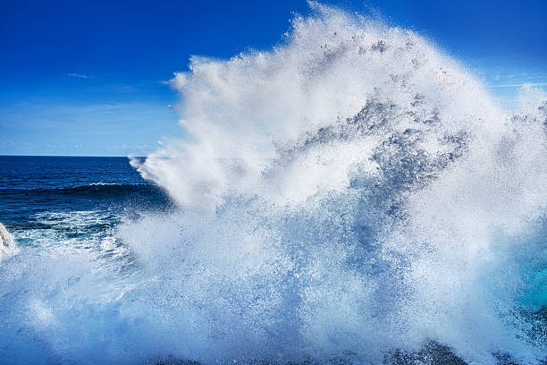 An intense ocean wave crashing and creating a dramatic, high splash against a vivid blue sky in Bali, showcasing the power and beauty of nature at its finest.