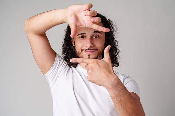 istock A young man with curly hair framing his face and making a gesture as if capturing a moment against a plain background 2226260836